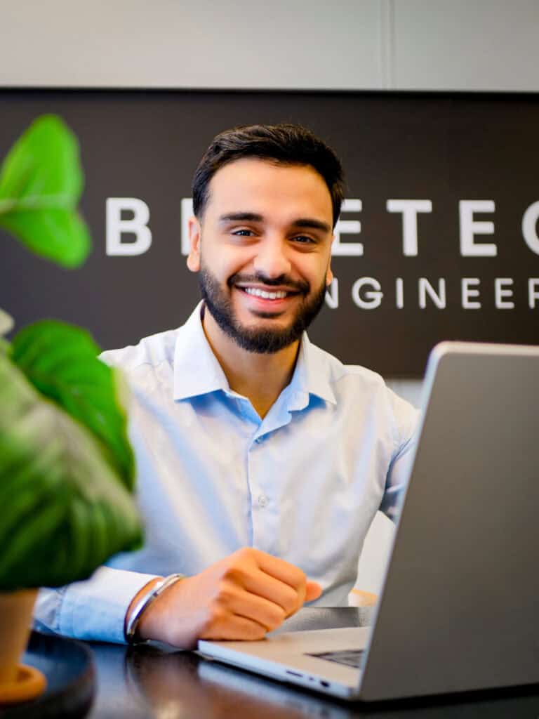 Onze professional Shiva zit achter een laptop in een kantooromgeving. Op de achtergrond zie je het Bluetech logo.